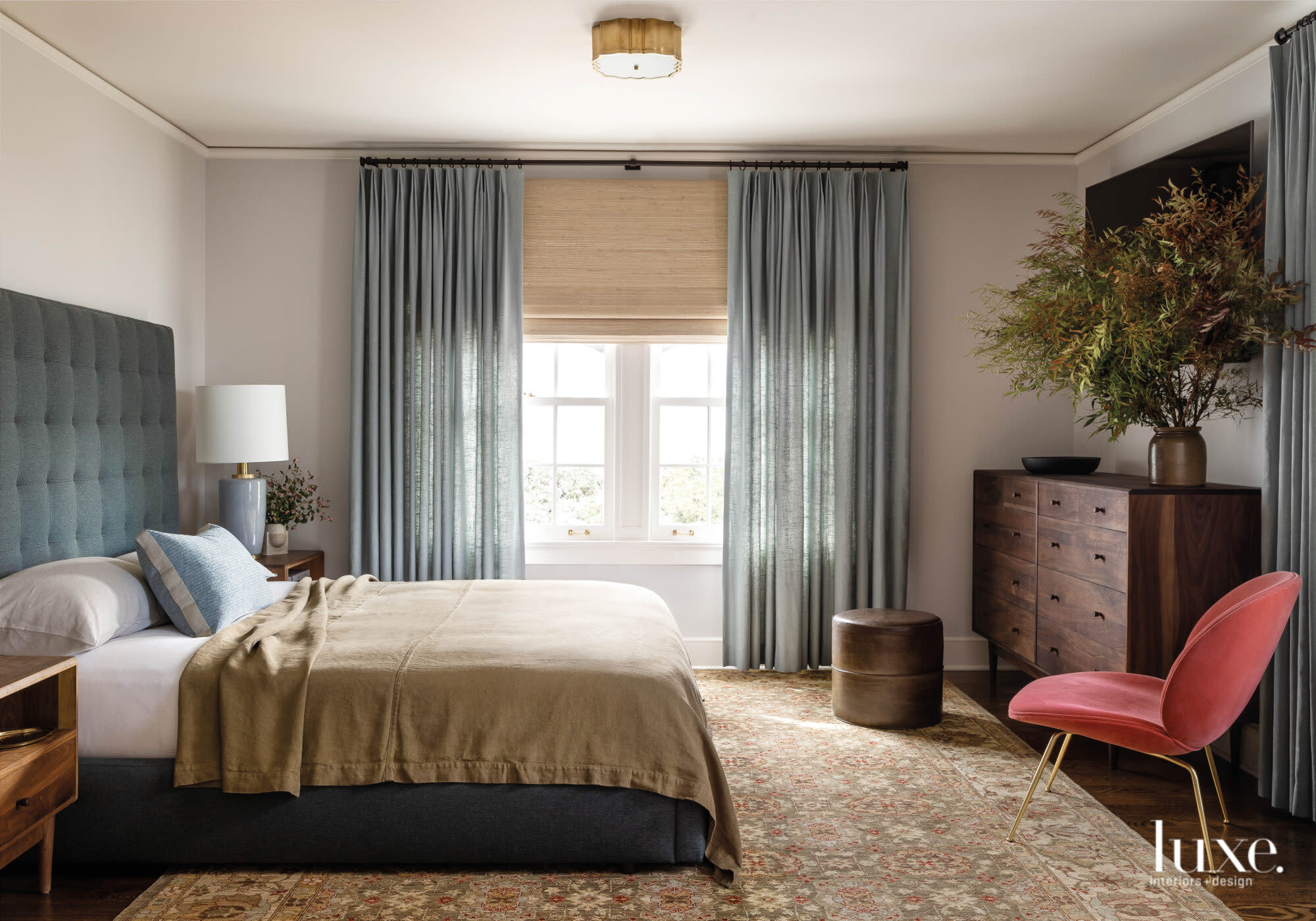 Master bedroom with bed with upholstered headboard and pink chair.