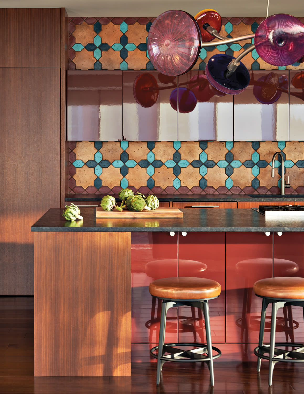 The kitchen has a copper and blue backsplash with orange stools in home by James Fung