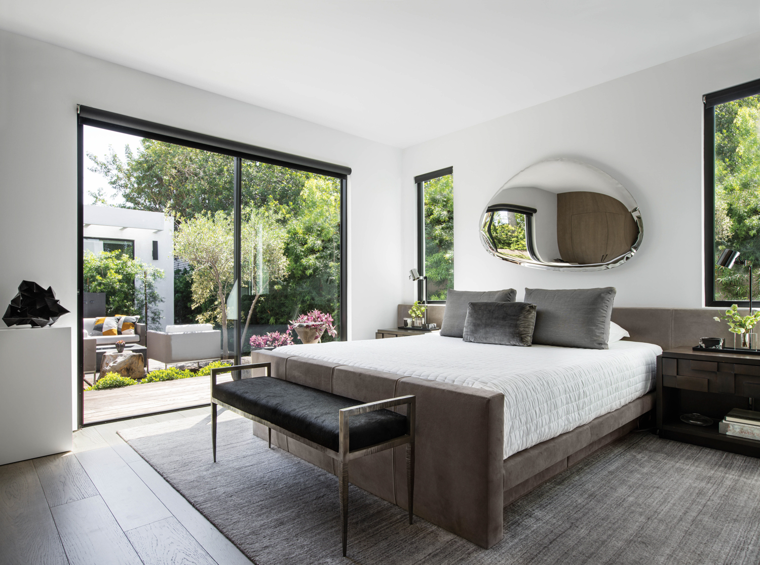 bedroom with minimalist bed, black bench, mirrored wall sculpture, and glass sliding doors by Jason Kalman