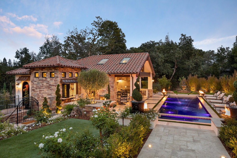 exterior of a pool house of a Northern California home with infinity edge pool, outdoor seating and a wrought iron fence by De Mattei Construction