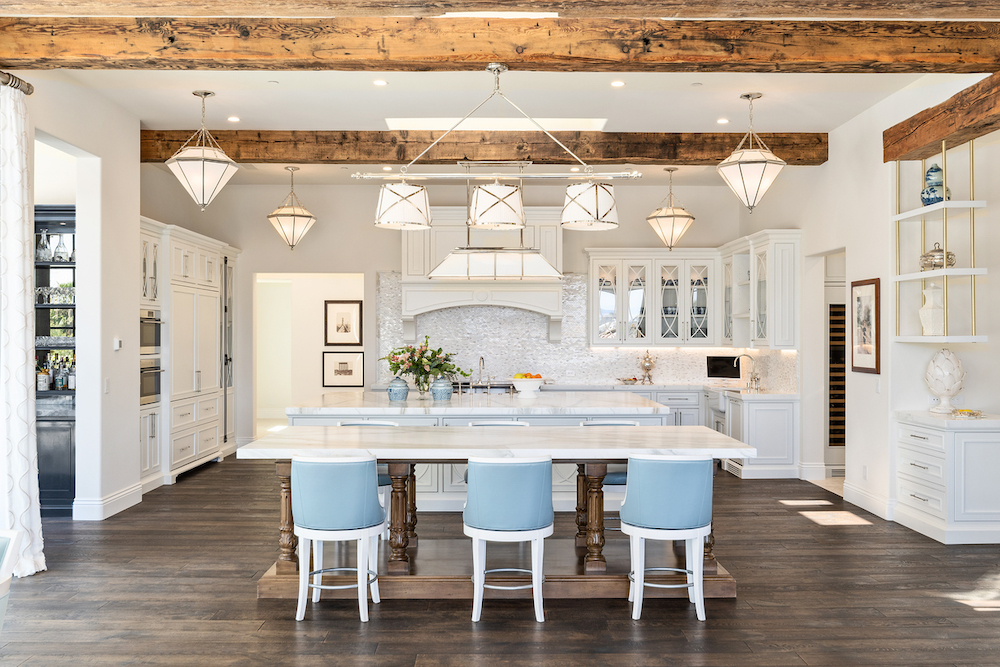 Interior of a kitchen showcasing white cabinets, blue bar stools and wooden beams.