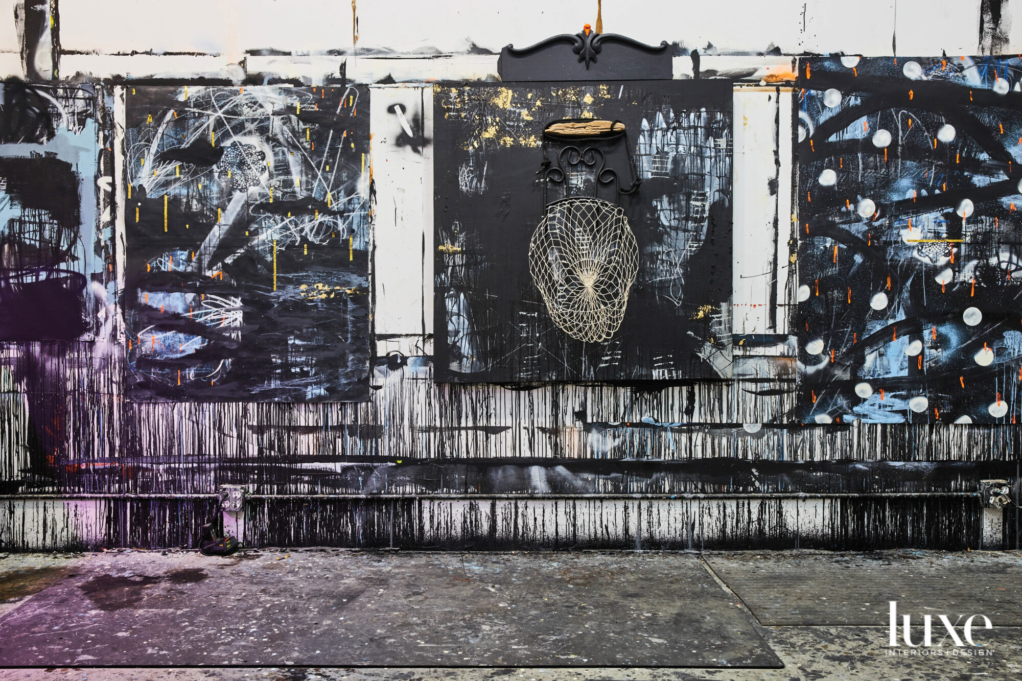 Interior of a room with paint-splattered concrete floors and three dark abstract paintings mounted along paint-splattered wall