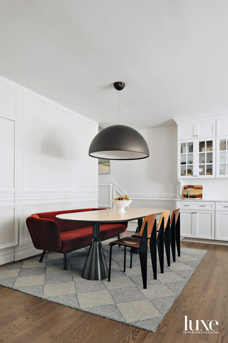 A dining room table surrounded by wood chairs and a red velvet sofa.