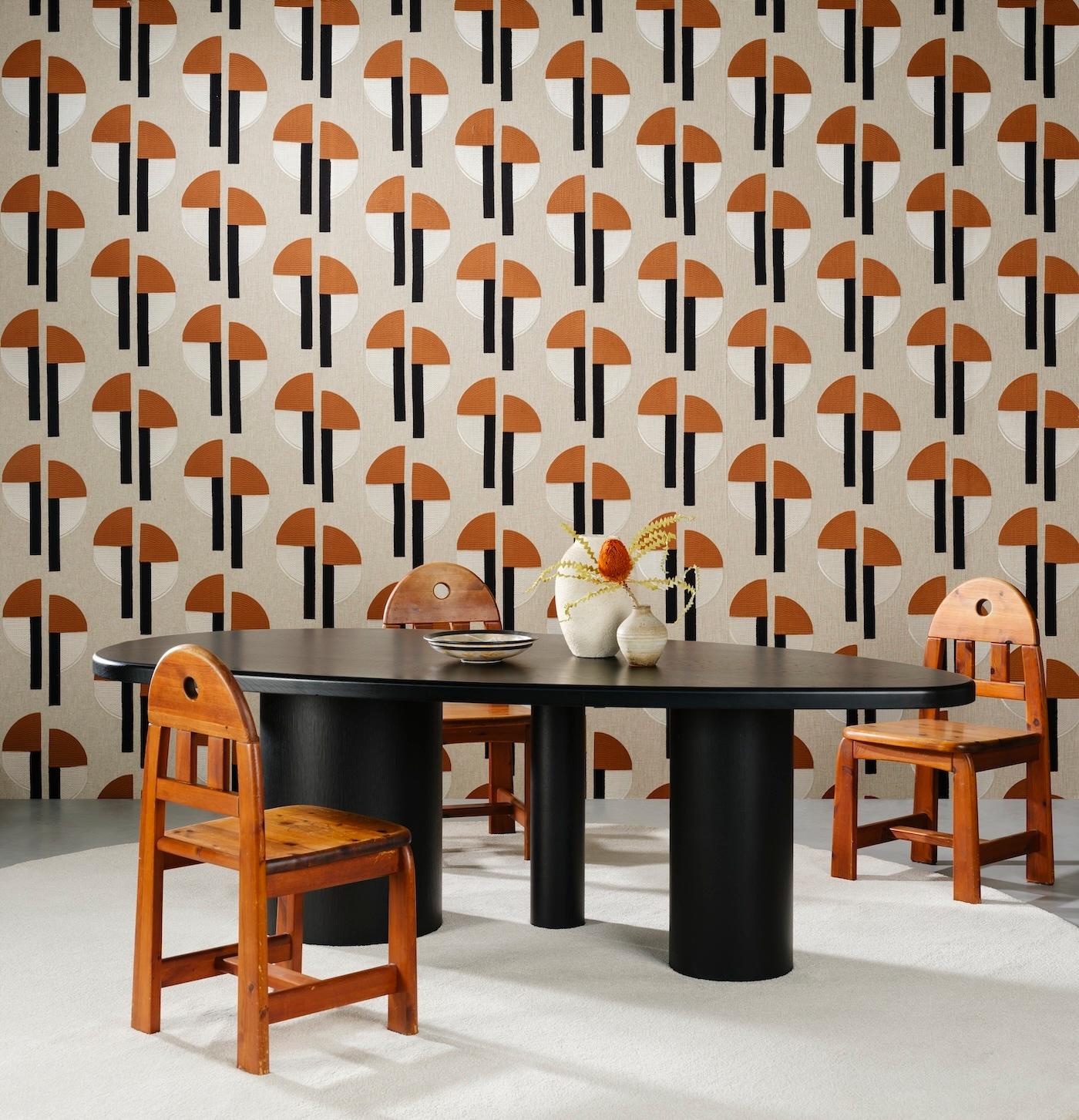 Retro dining room with a black oval table, surrounded by four wooden chairs. The background features a bold geometric orange and black patterned wallpaper.