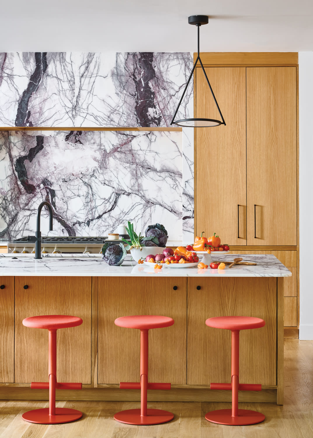modern kitchen with a marble backsplash and red barstools lining an island