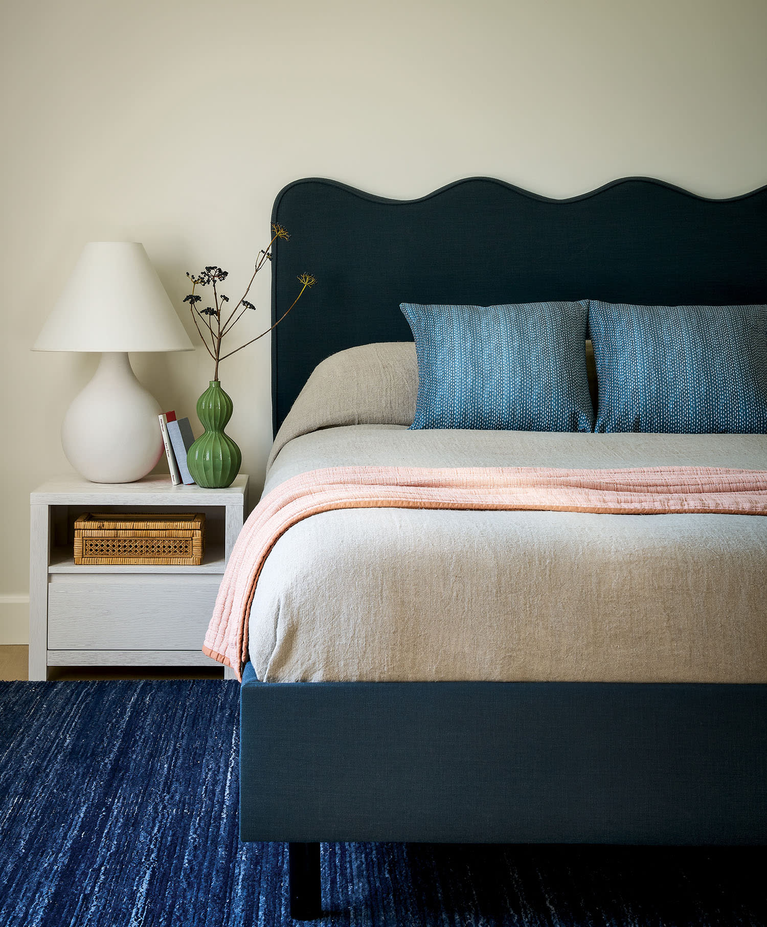 A bed with a blue headboard beside a white nightstand, creating a cozy and stylish bedroom setting.