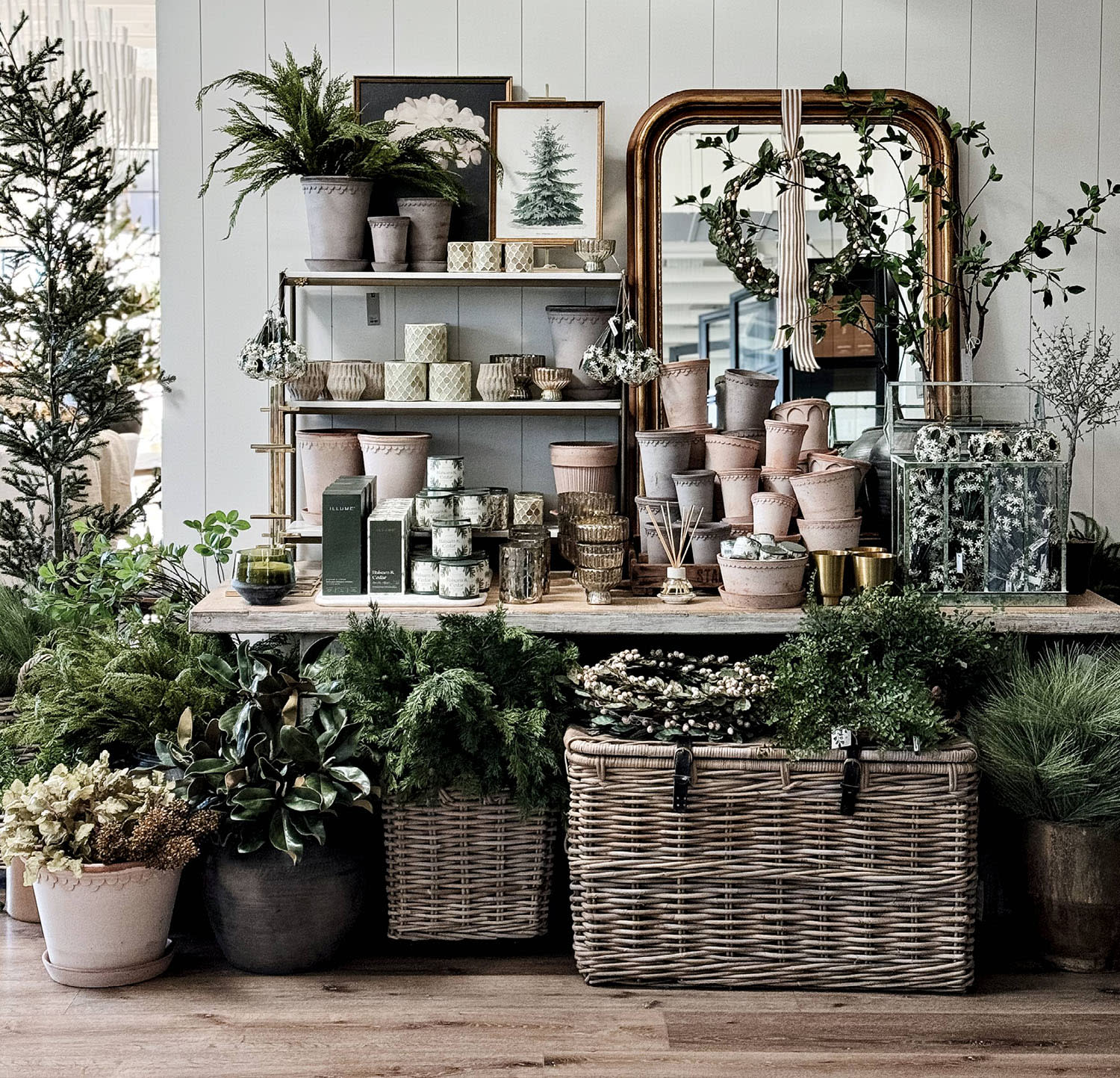 Bowls and other pottery stacked on a table decorated with a mirror and festive holiday greenery.