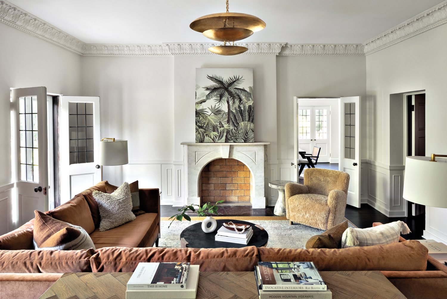 White living room with terracotta sectional, a palm artwork on a marble fireplace and brass pendant