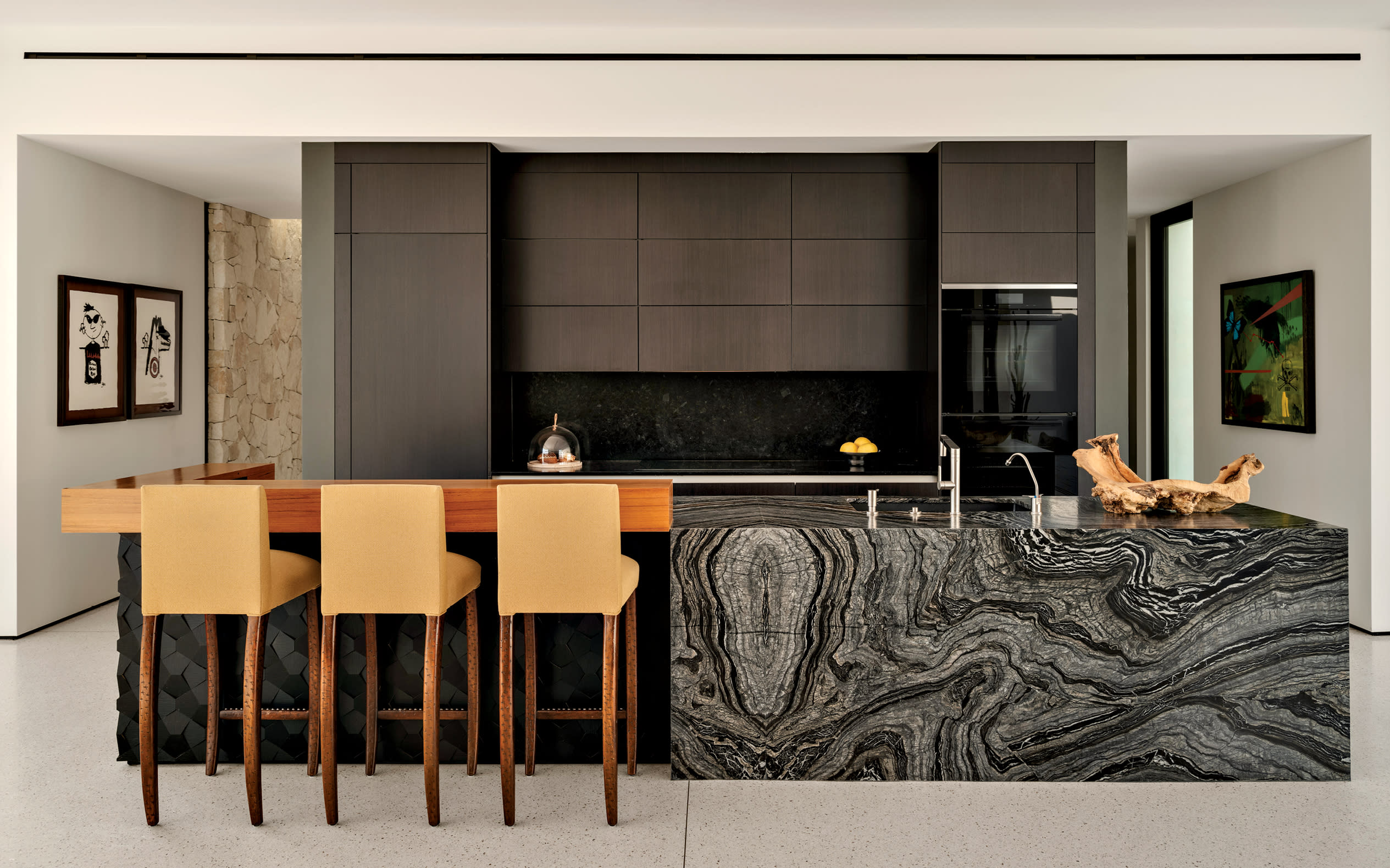 kitchen with a richly veined leathered marble island flanked by 3 bar seats and dark wood cabinetry