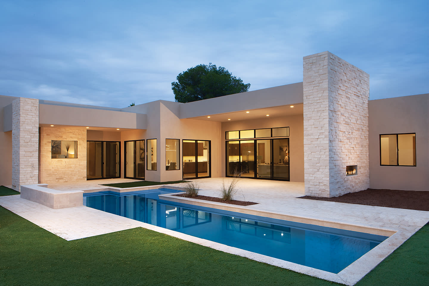 Modern desert home with lap pool and stone chimney at dusk