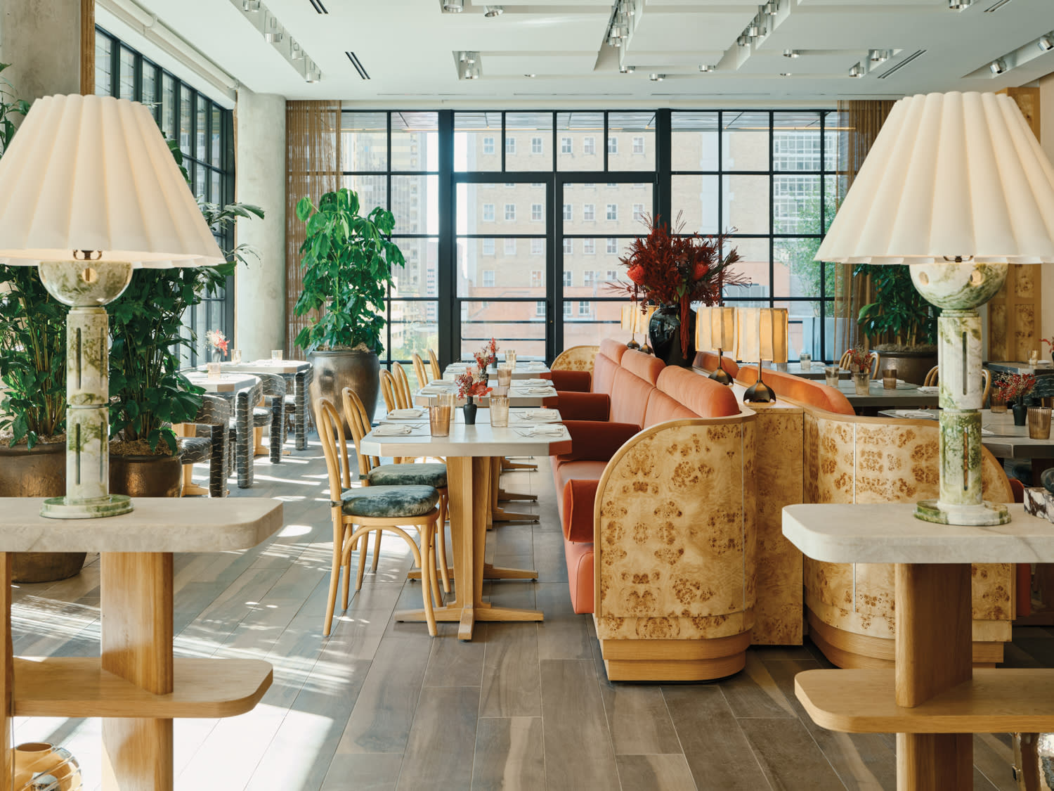 Floor-to-ceiling steel-framed windows backdrop two long curved burl-wood banquettes with pink velvet