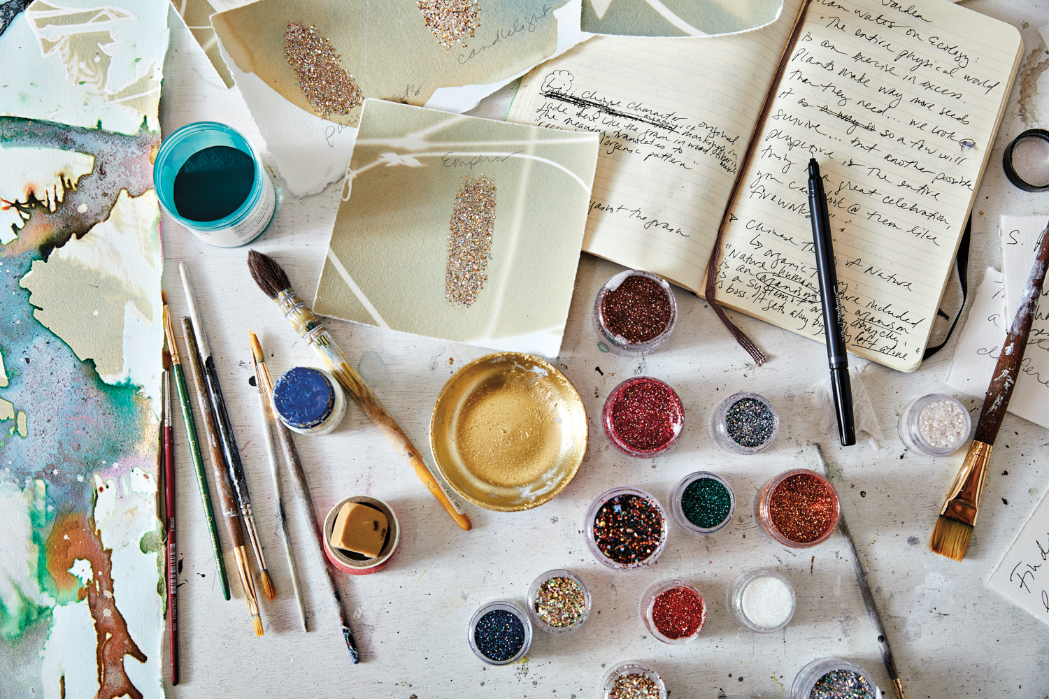 Table with notebooks, paint brushes and colorful pots