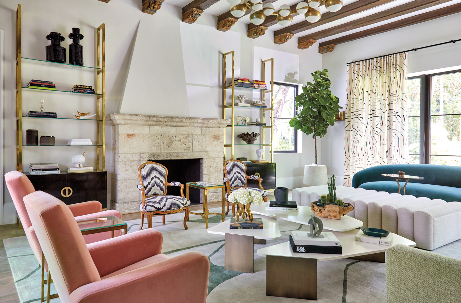 living area with pink armchairs, antique fireplace, teal sofa, white tables and gold étagères