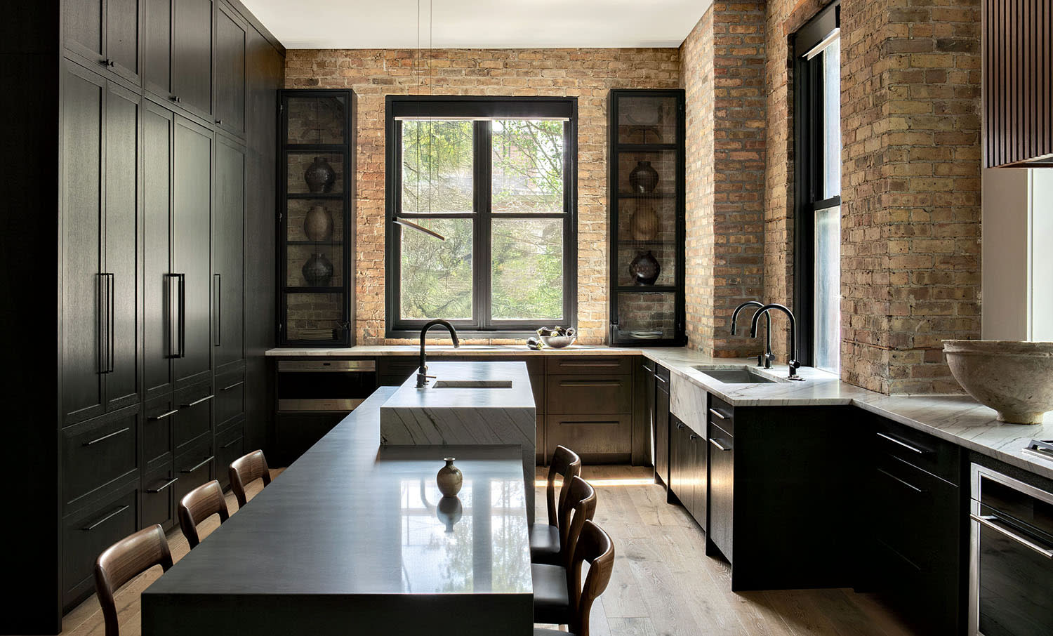 A kitchen with brick walls, wood cabinets and stone countertops, set up with a table and chairs.