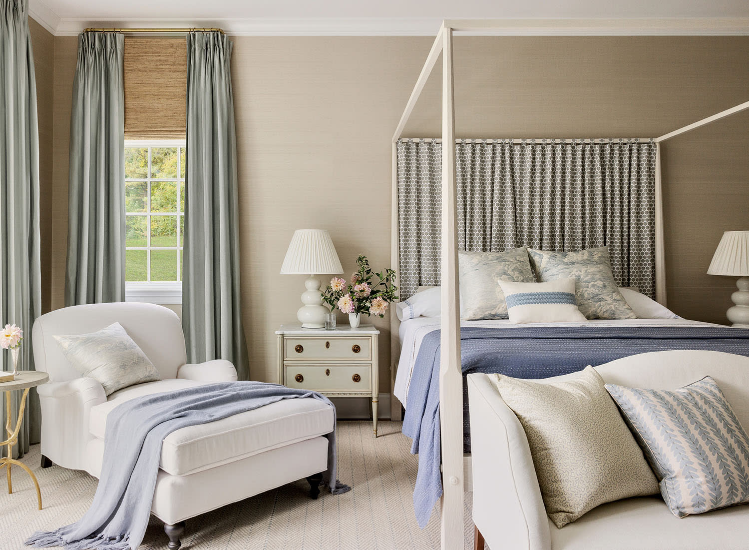 Elegant bedroom with a four-poster bed, light blue bedding, and matching curtains. A cozy armchair with a throw is nearby. Soft, calming atmosphere.