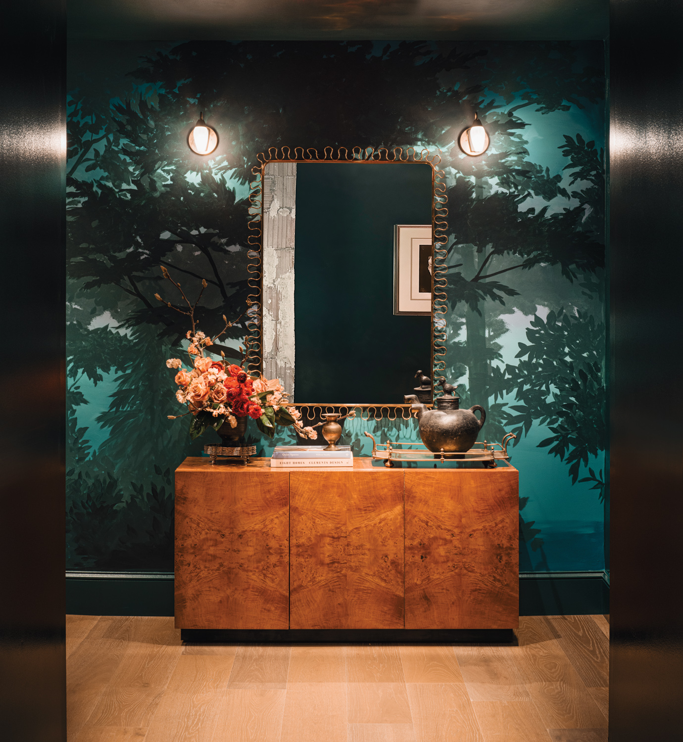 Forest-inspired wall mural in shades of green behind a mirror and wood console