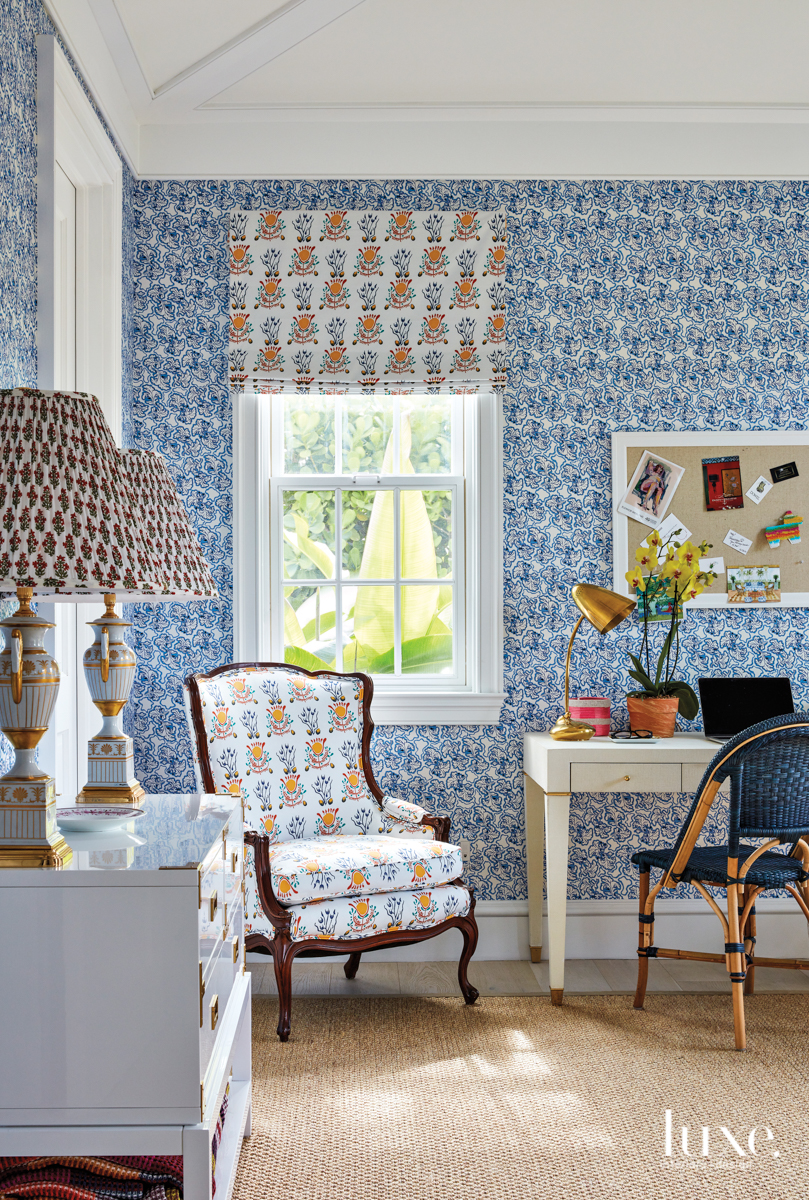 colorful office with blue floral wallpaper, patterned armchair, tan desk and blue office chair