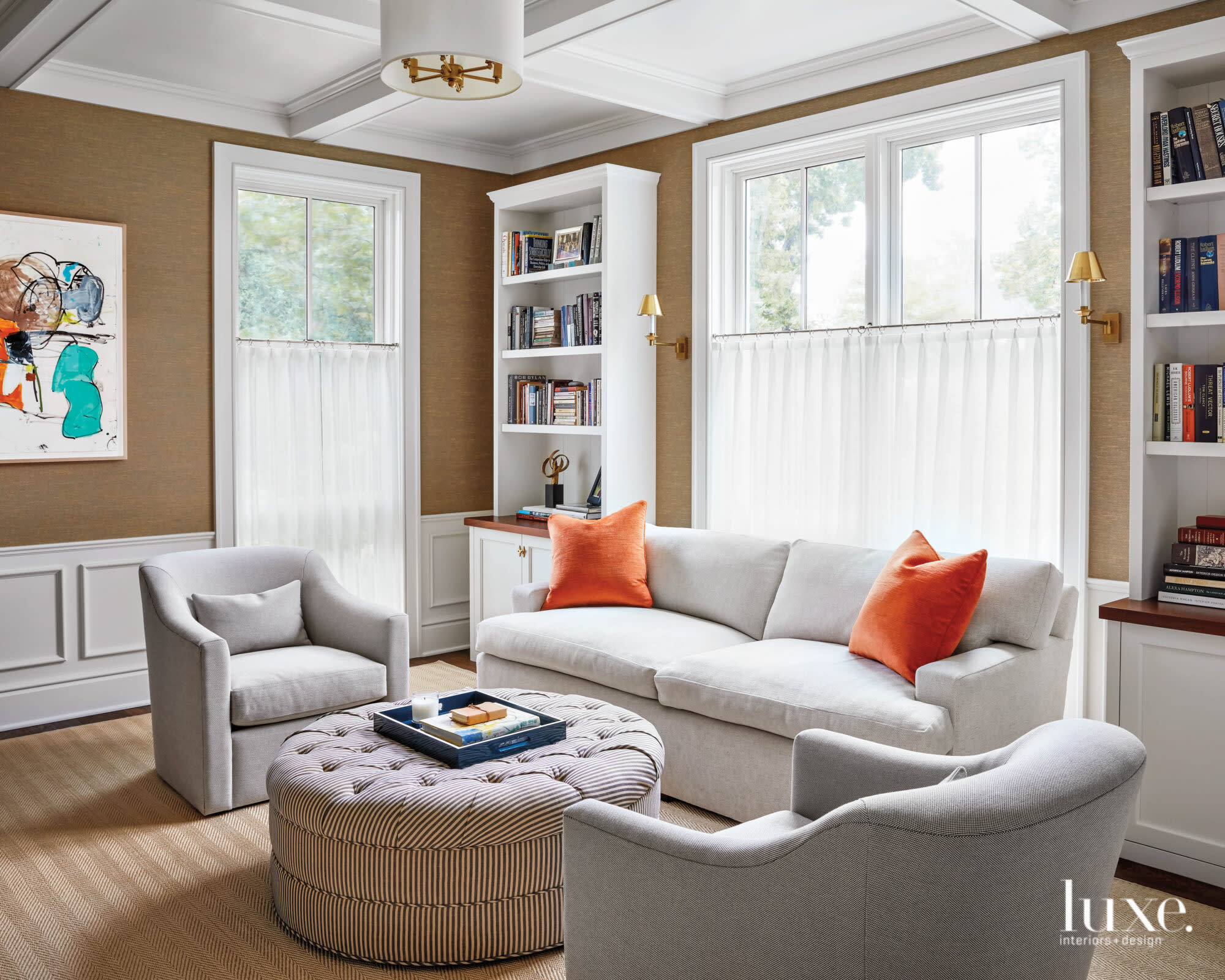 white sitting area off study with neutral seating, orange throw pillows, striped ottoman