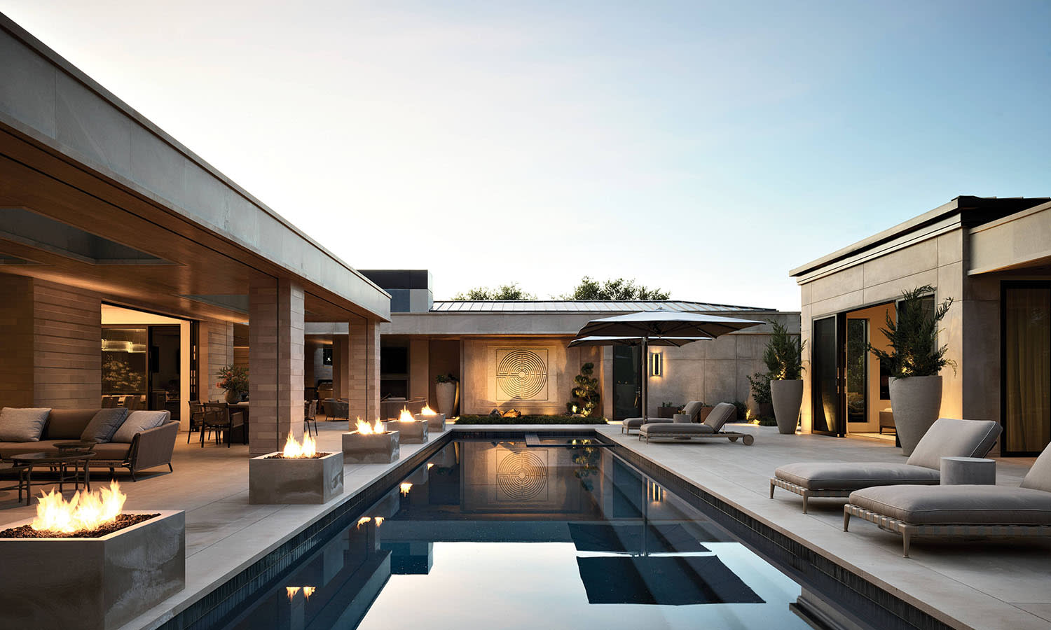 contemporary home's outdoor pool lined with daybeds and fire pits