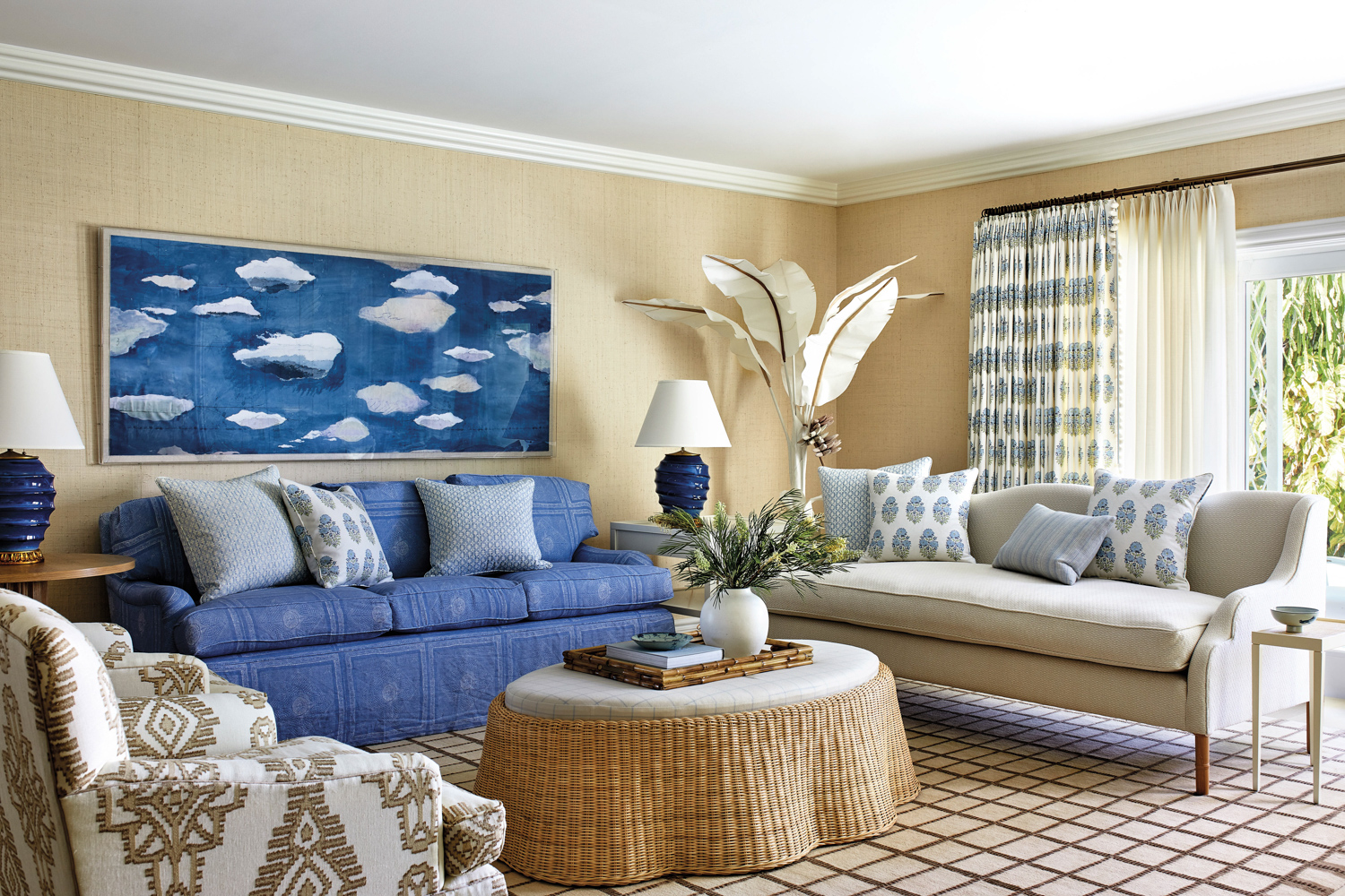 living room with tan ottoman, blue couch, cloud painting and white lamp in home by Cameron Ruppert