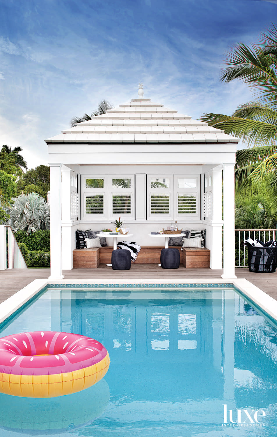 pool deck with white cabana outfitted with bench, white tables and black ottomans