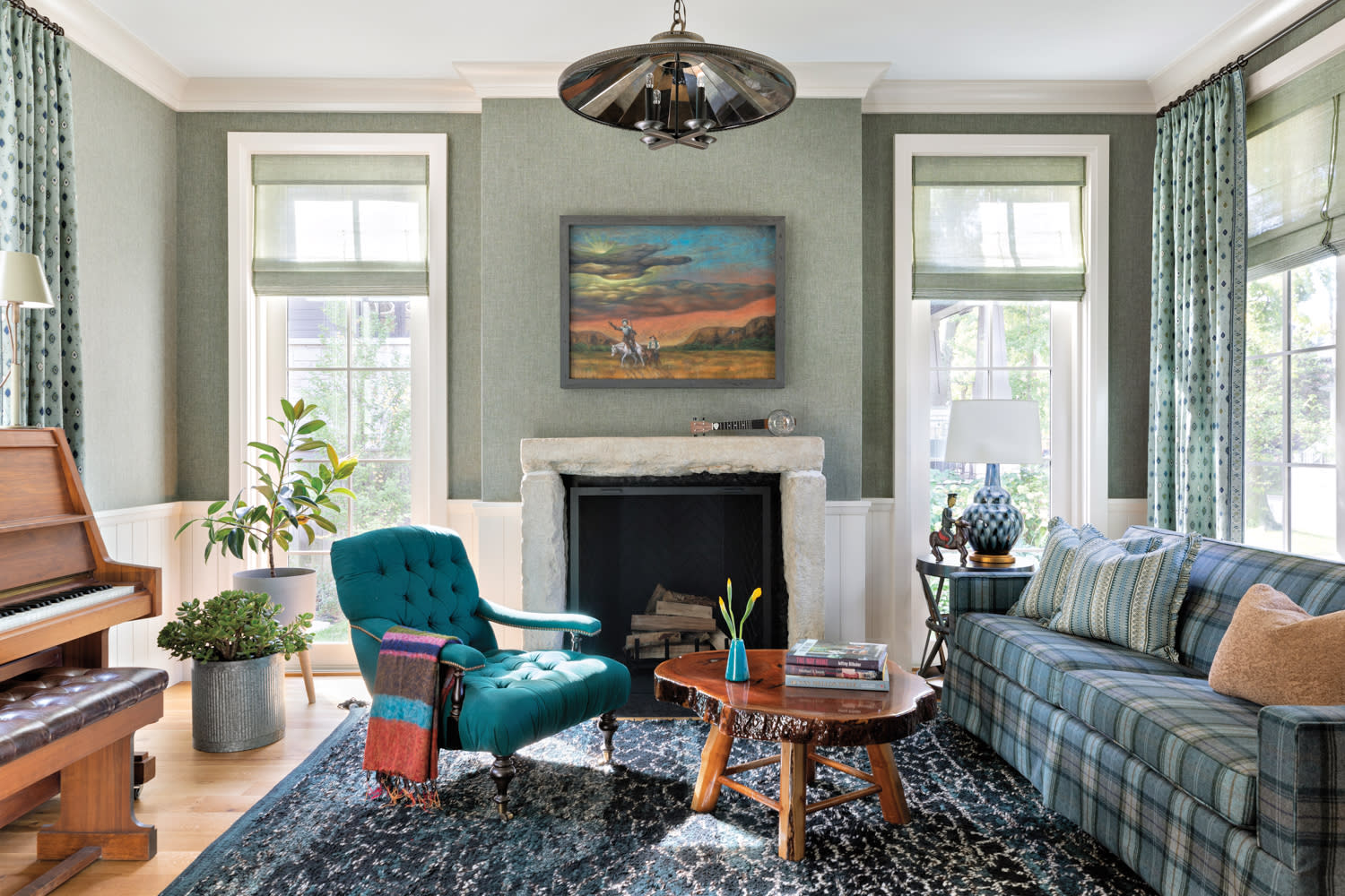 A green living room with piano, stone fireplace, blue plaid couch and teal armchair