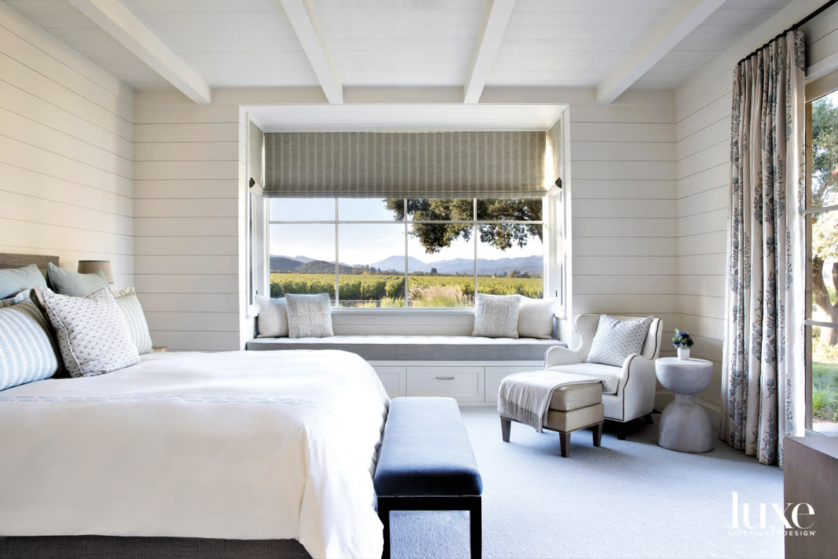 A bedroom features a large window and windowseat that overlook the vineyards.