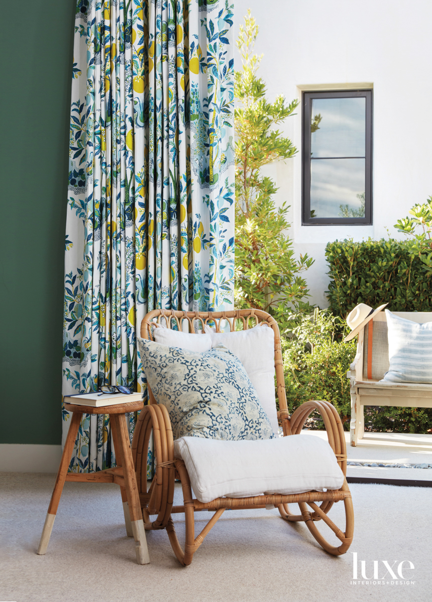 Detail of room with green wall, floral drapery and wicker chair