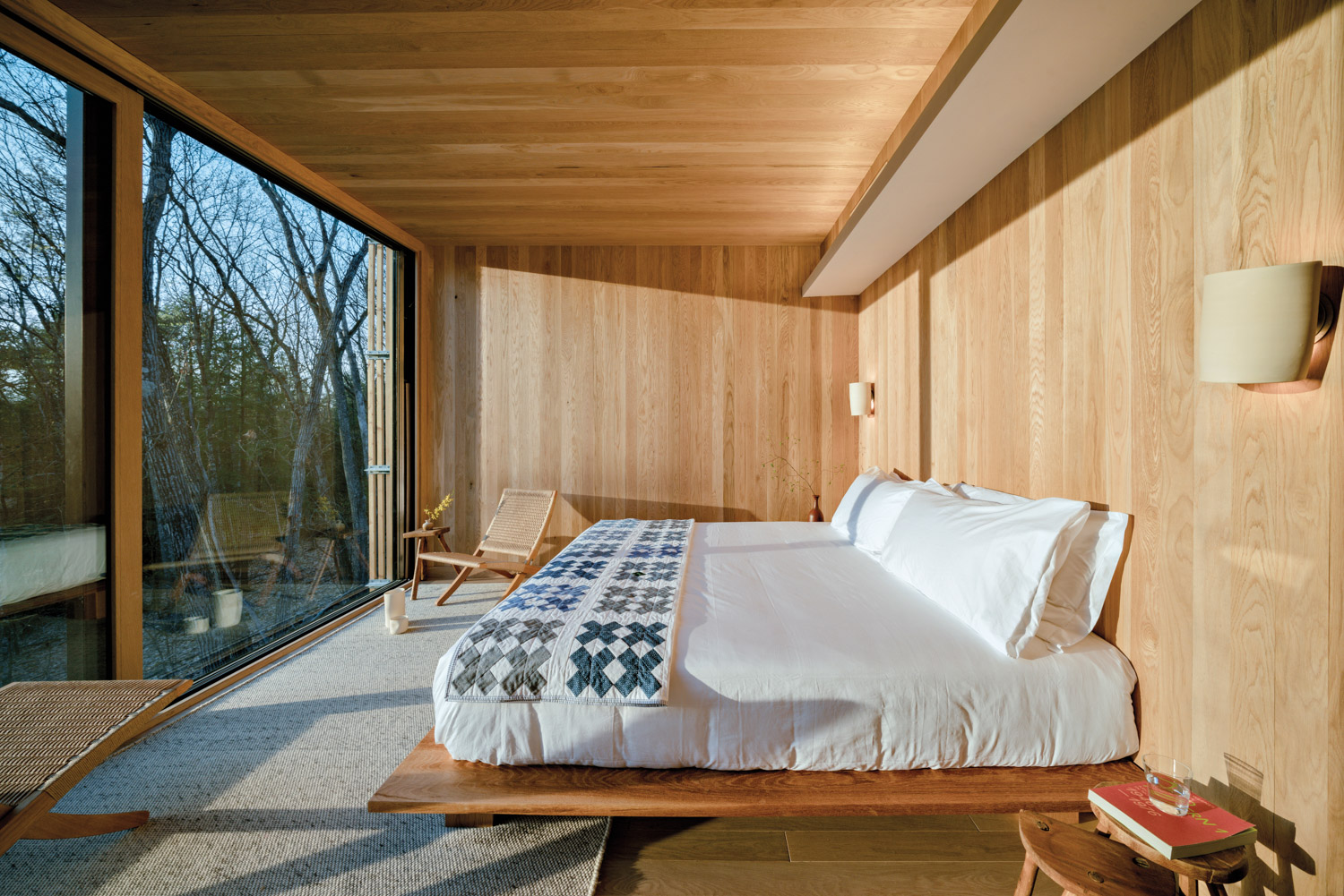 White bed in wood-clad cabin with a large glass window