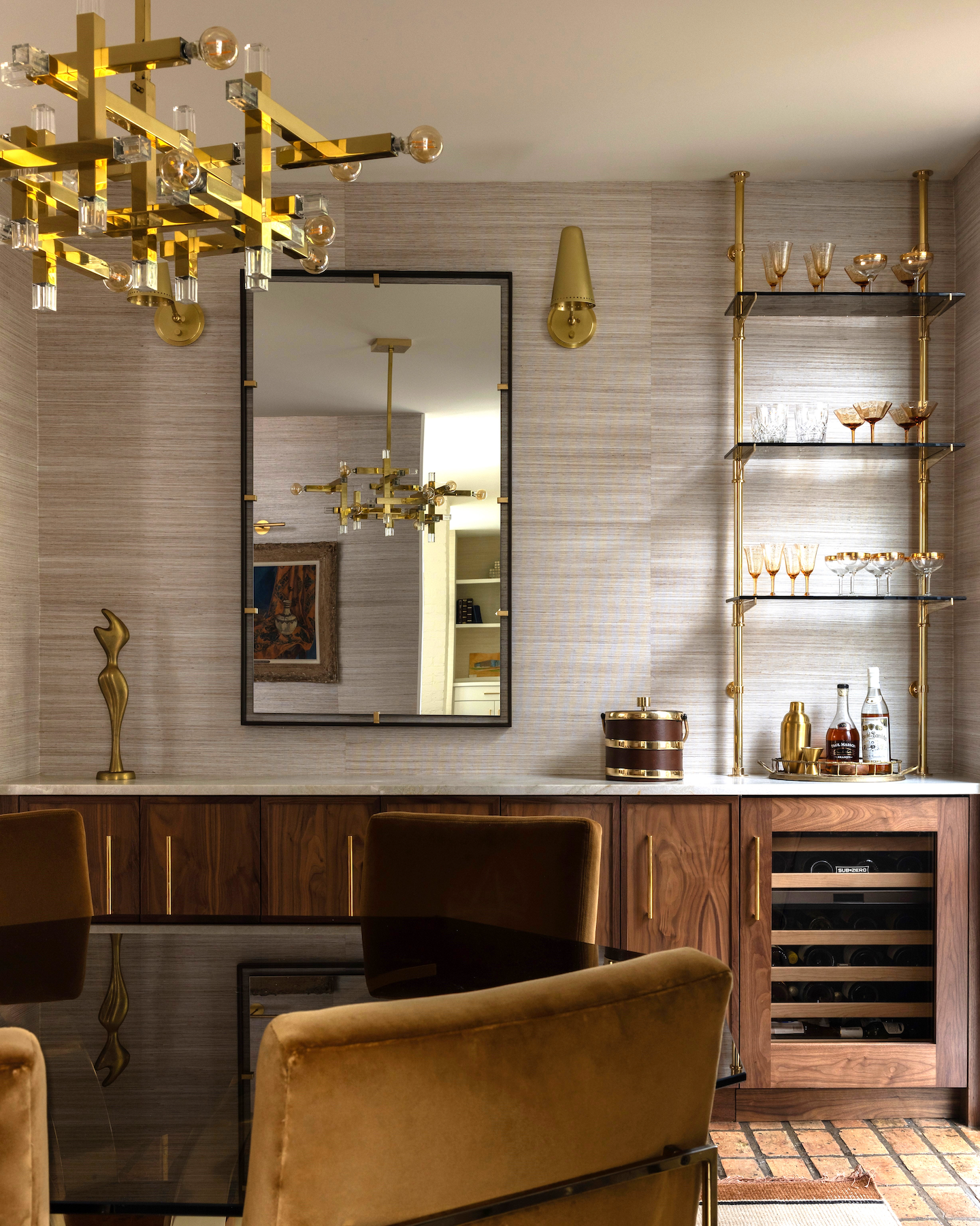 A moody palette and polished brass accents elevate this intimate dining space. Custom walnut cabinetry, vintage inspired glassware, and a statement chandelier from Visual Comfort create a space that's both warm and refined.