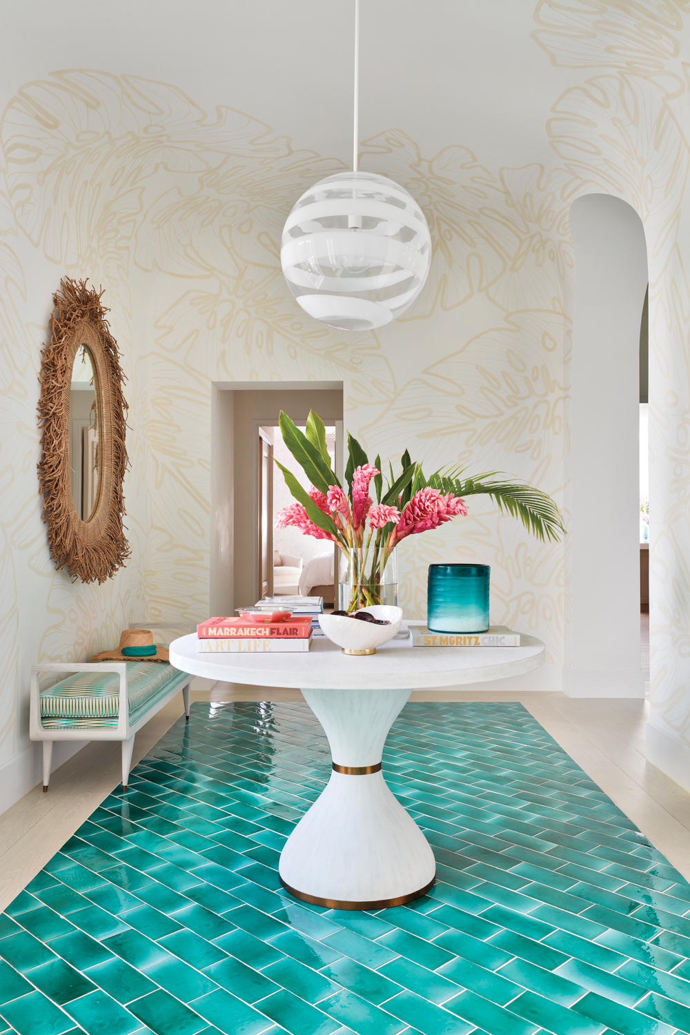 foyer with palm leaf mural, round white table, white globe pendant and teal glazed-tile flooring