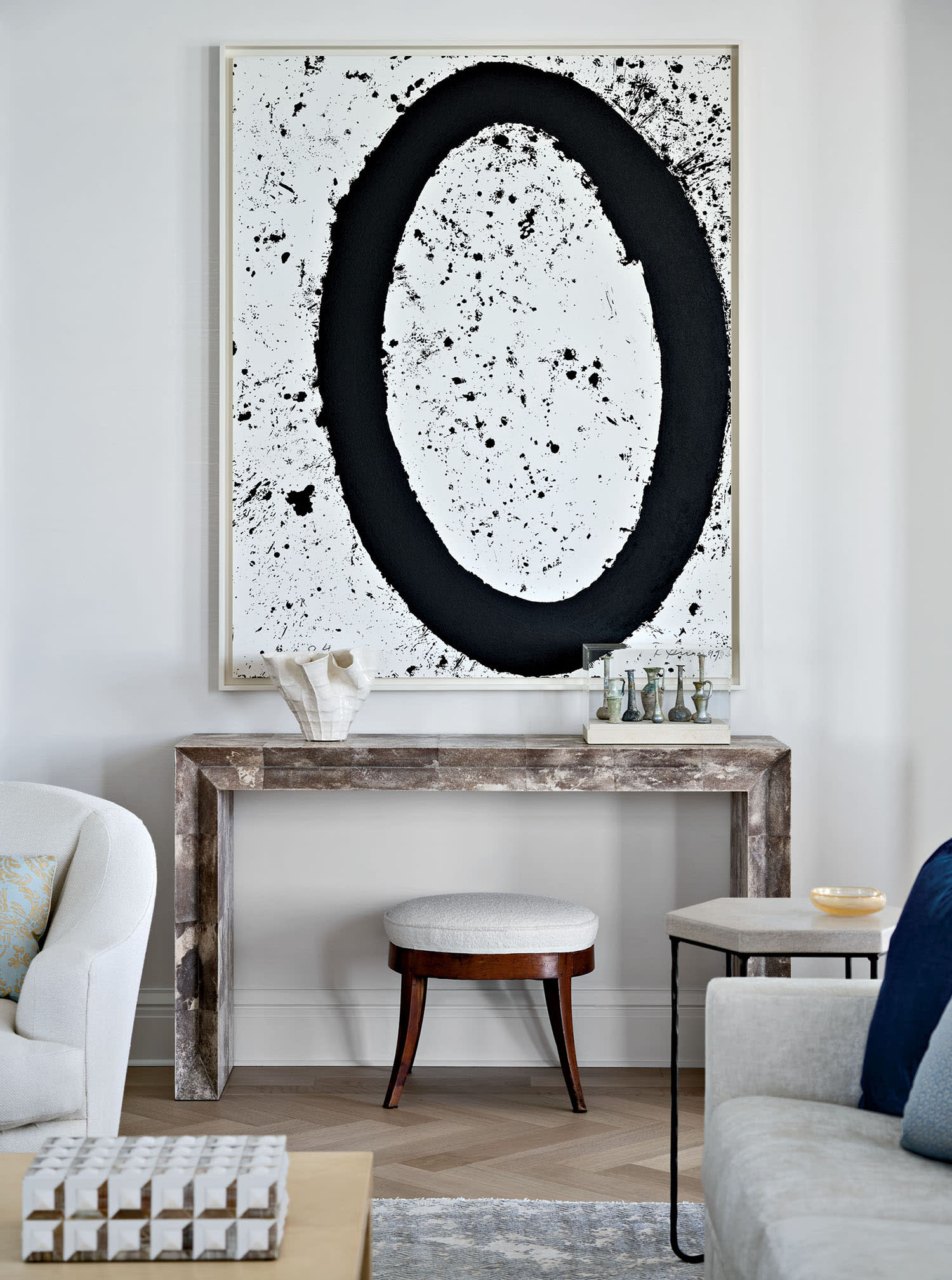 A console table sits against a wall with a small stool nestled beneath, set beneath abstract artwork.