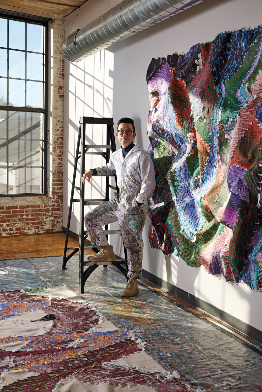 Kenny Nguyen standing on concrete floor next to a ladder and colorful wall hanging