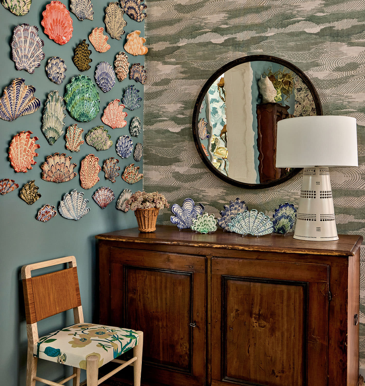 Colorful ceramic seashells hang on a blue wall near a mirror and side chest.