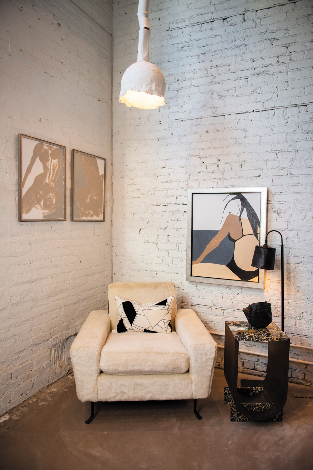 Shop with whitewashed brick walls, cream armchair and neutral-colored art.