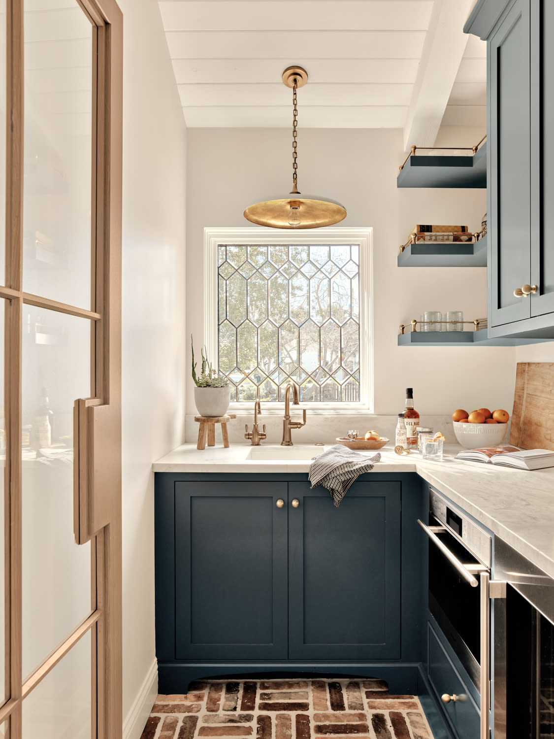 Pantry with dark blue cabinetry, white marble countertops and brick flooring