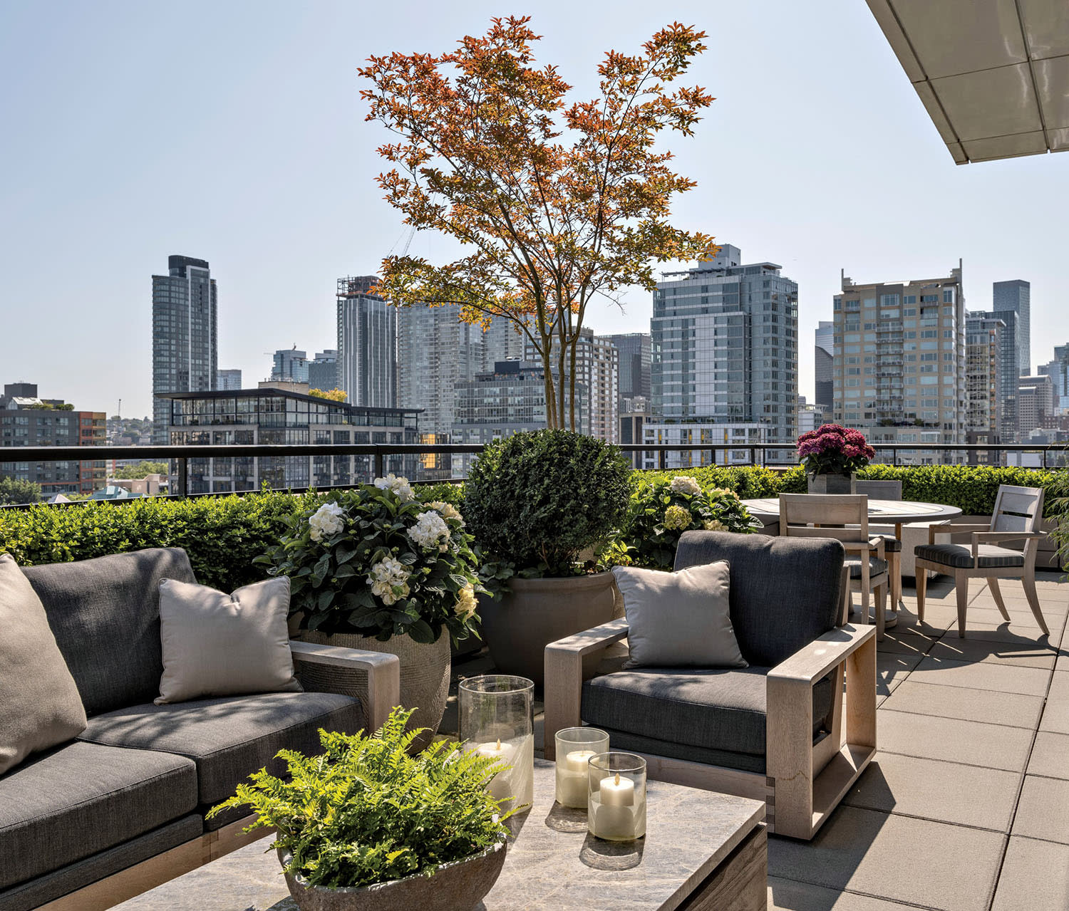 Rooftop terrace with modern gray furniture set against a skyline of tall buildings under a clear blue sky