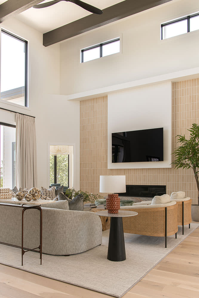 Mid-century modern meets transitional design in this airy, lightfilled space. Soaring two-story ceilings and a striking tiled accent wall create a sense of grandeur, while warm, earthy tones and curated furnishings craft a grounded yet contemporary feel. Photography by Strictly Natural Light.