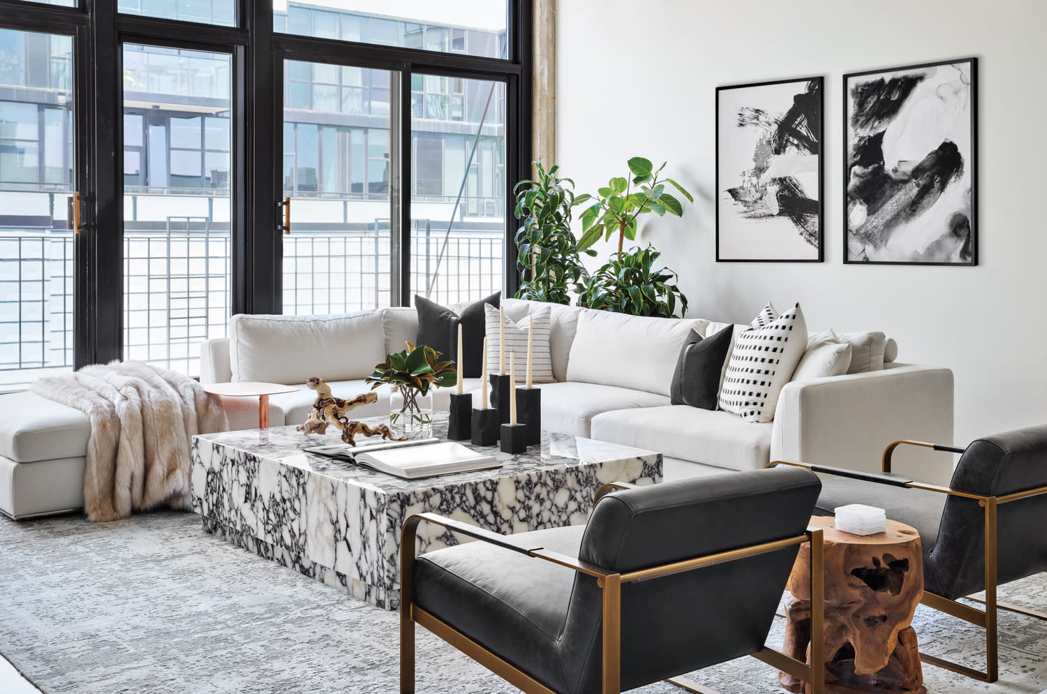 A living room with a white sectional, two black leather chairs and a marble cocktail table.