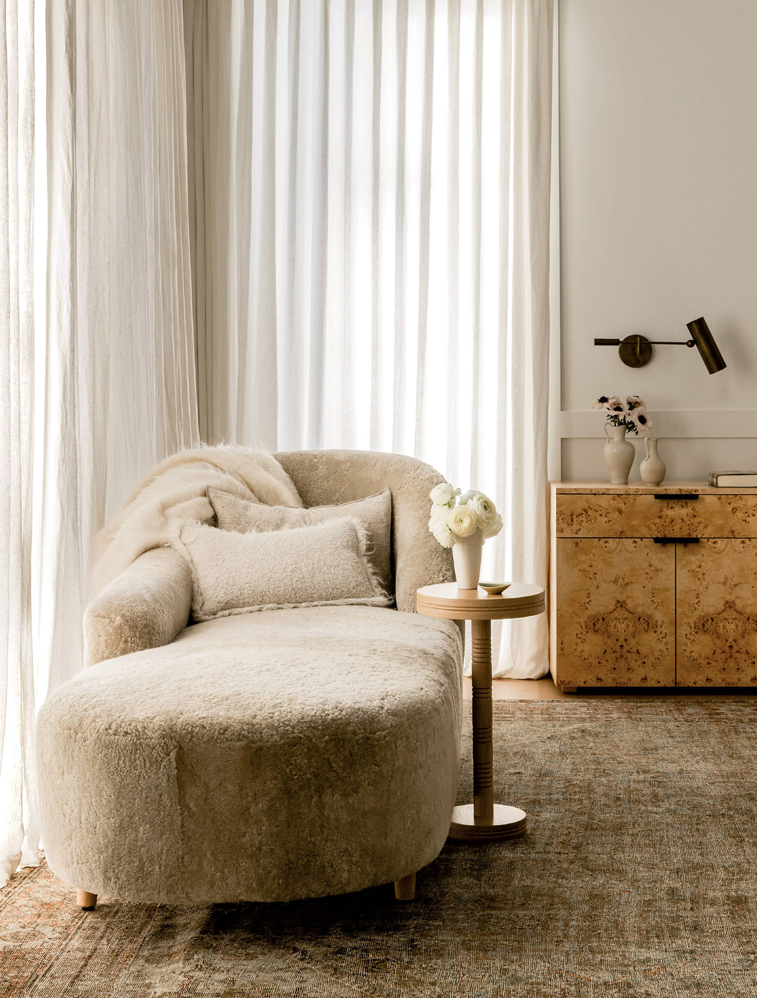 A chaise lounge with pillows and a matching throw blanket sit near a window with the curtains drawn.
