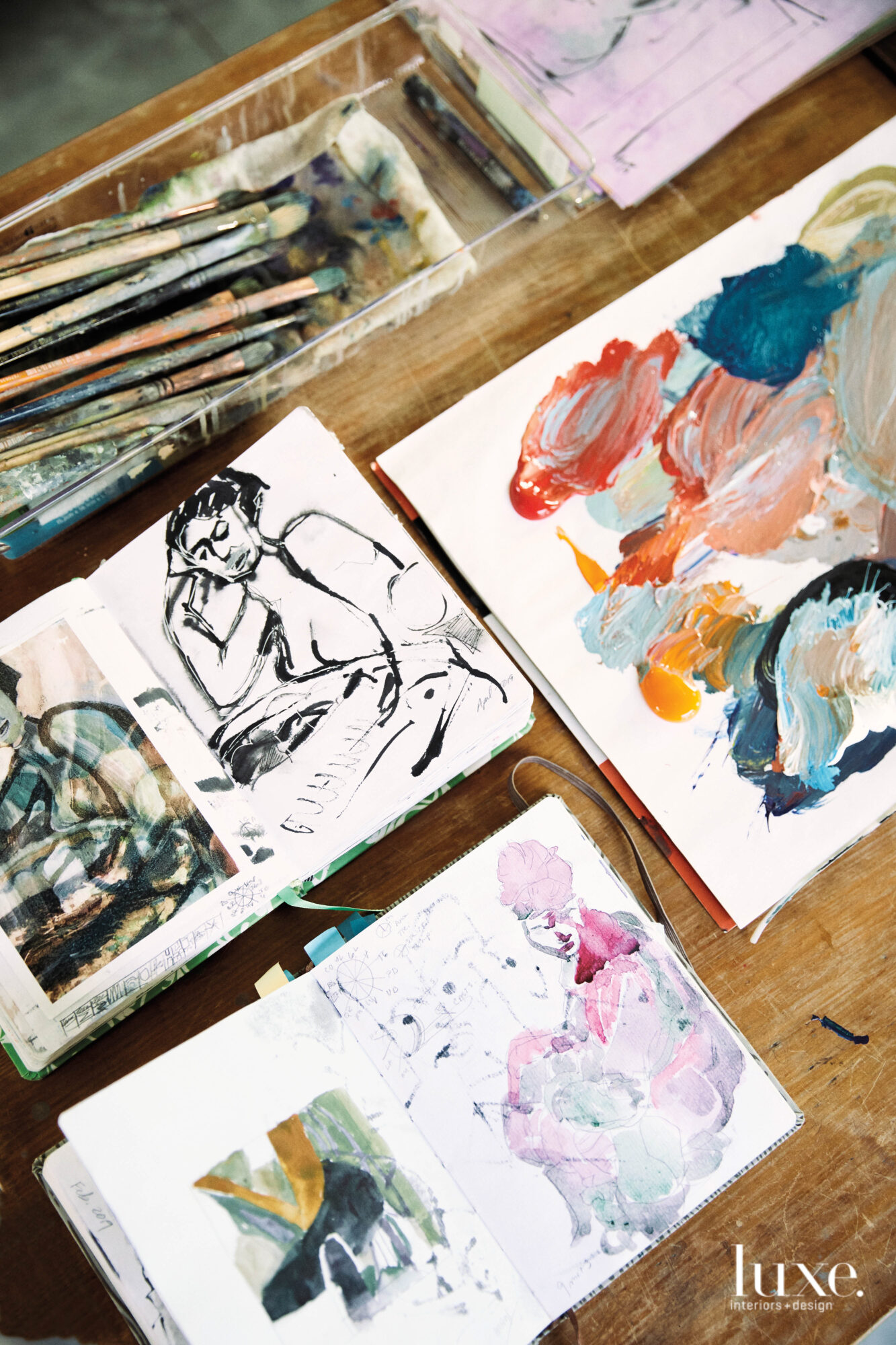 Studies of figurative paintings in small notebooks, a collection of paintbrushes, a makeshift palette topped with mixed pigments