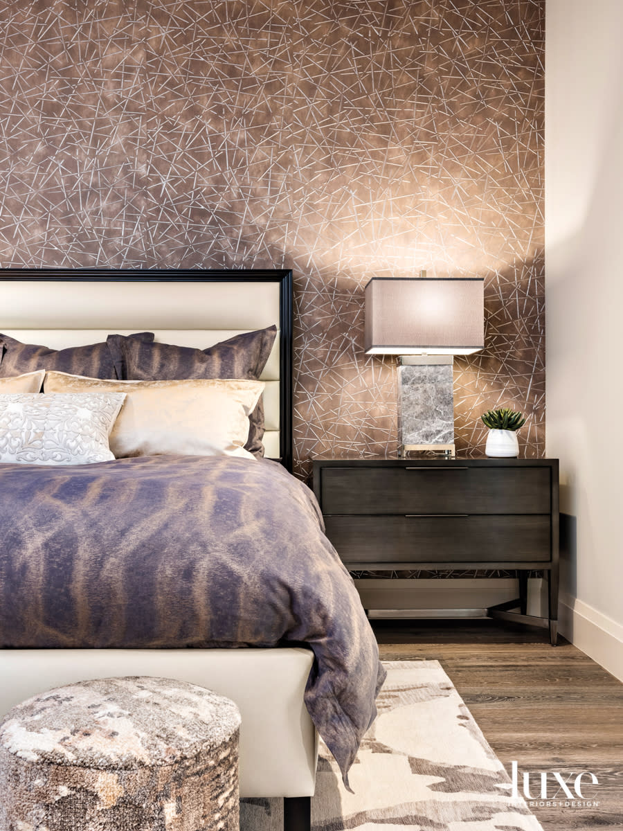 A bedroom with geometric wallpaper and a leather-upholstered bed.