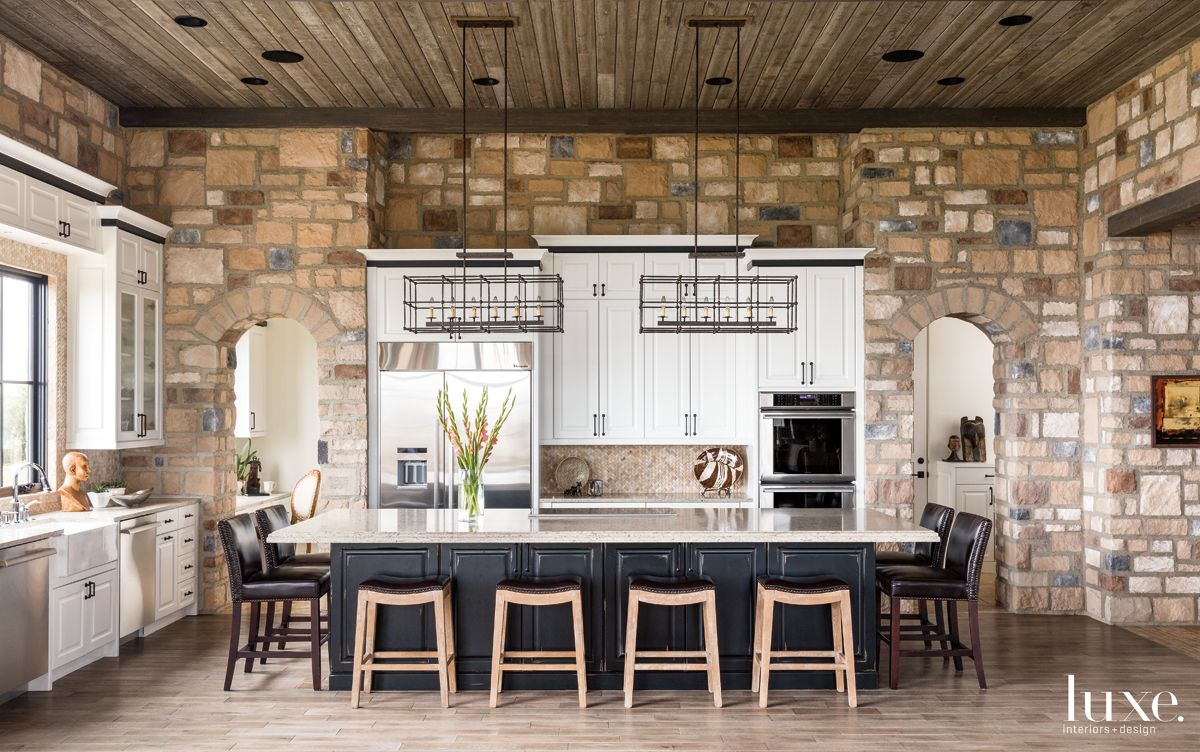 kitchen that features white cabinetry that plays off brick and stone walls and counters