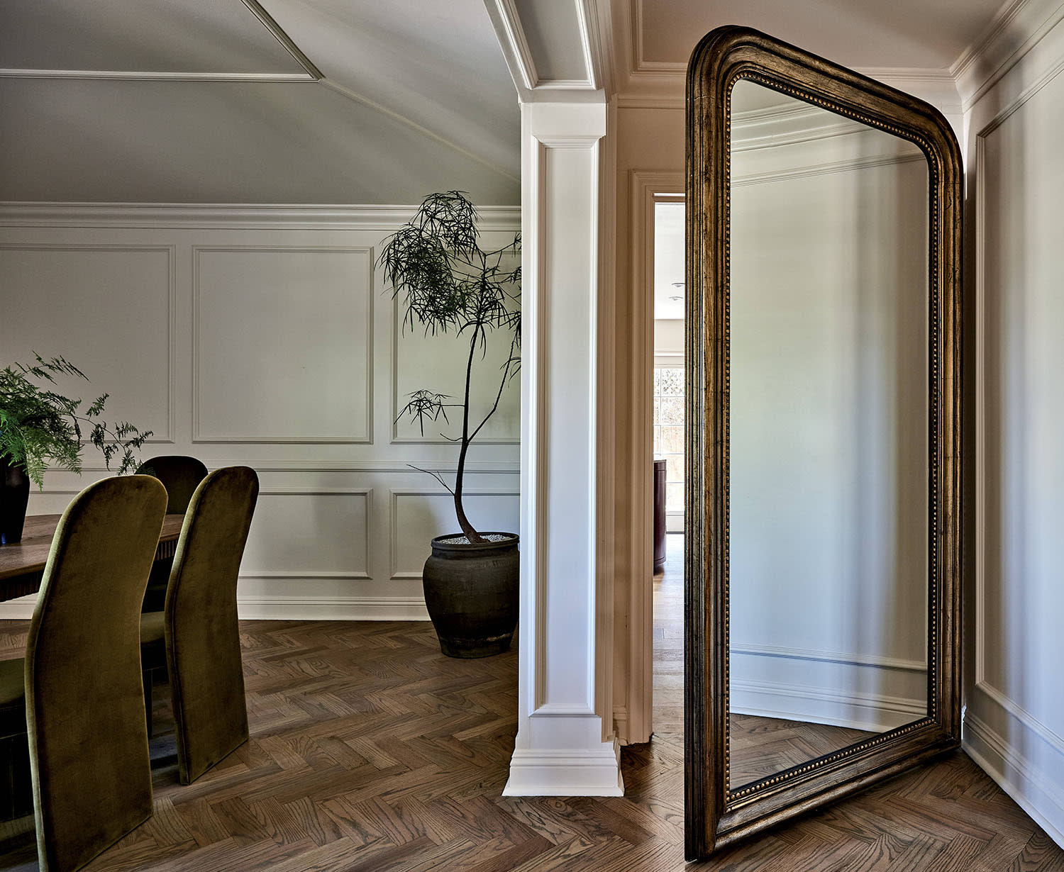 A space behind the dining room table with a mirrored door and a large planter holding a tree nearby.