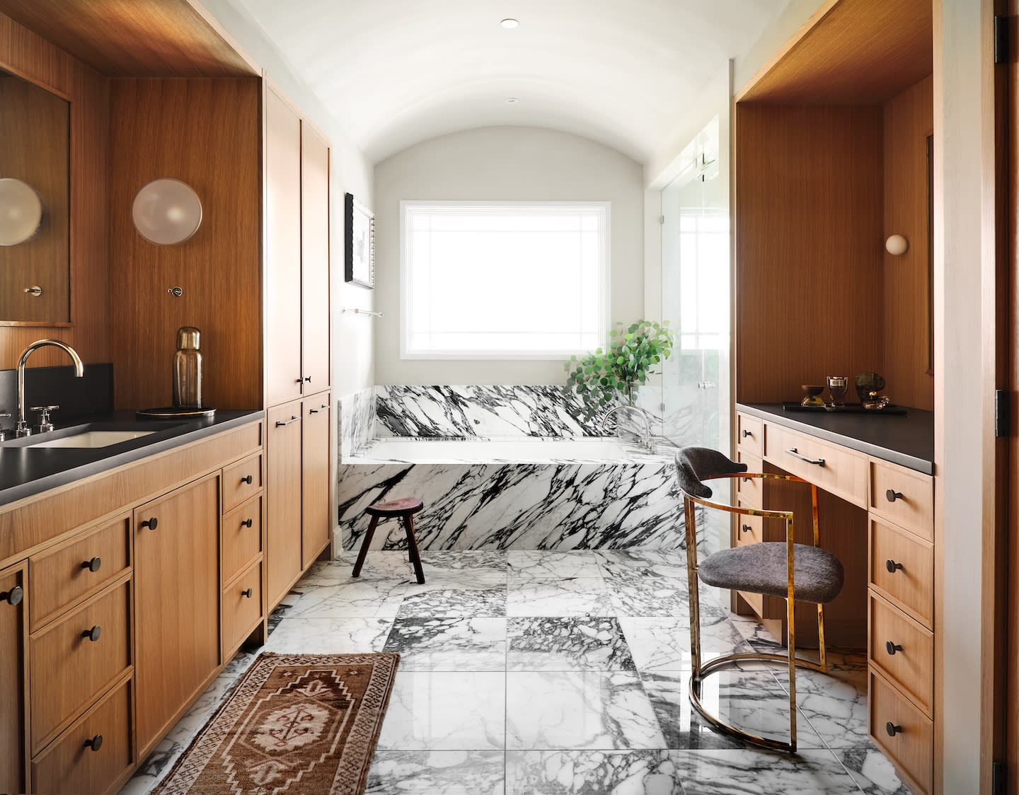 Spacious bathroom with marble walls and floors, wooden cabinetry, a large window, and a potted plant by the bathtub. Elegant and serene atmosphere.