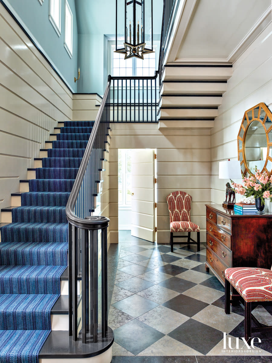 A blue rug on stairs in foyer that has a black-and-white checkered floor.