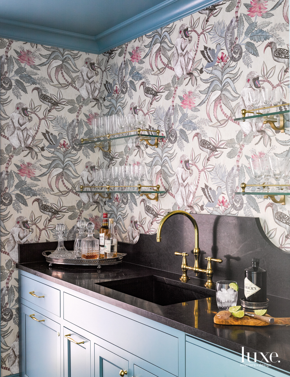 butler's pantry with plant and birds patterned wallpaper, blue cabinetry and black marble countertop