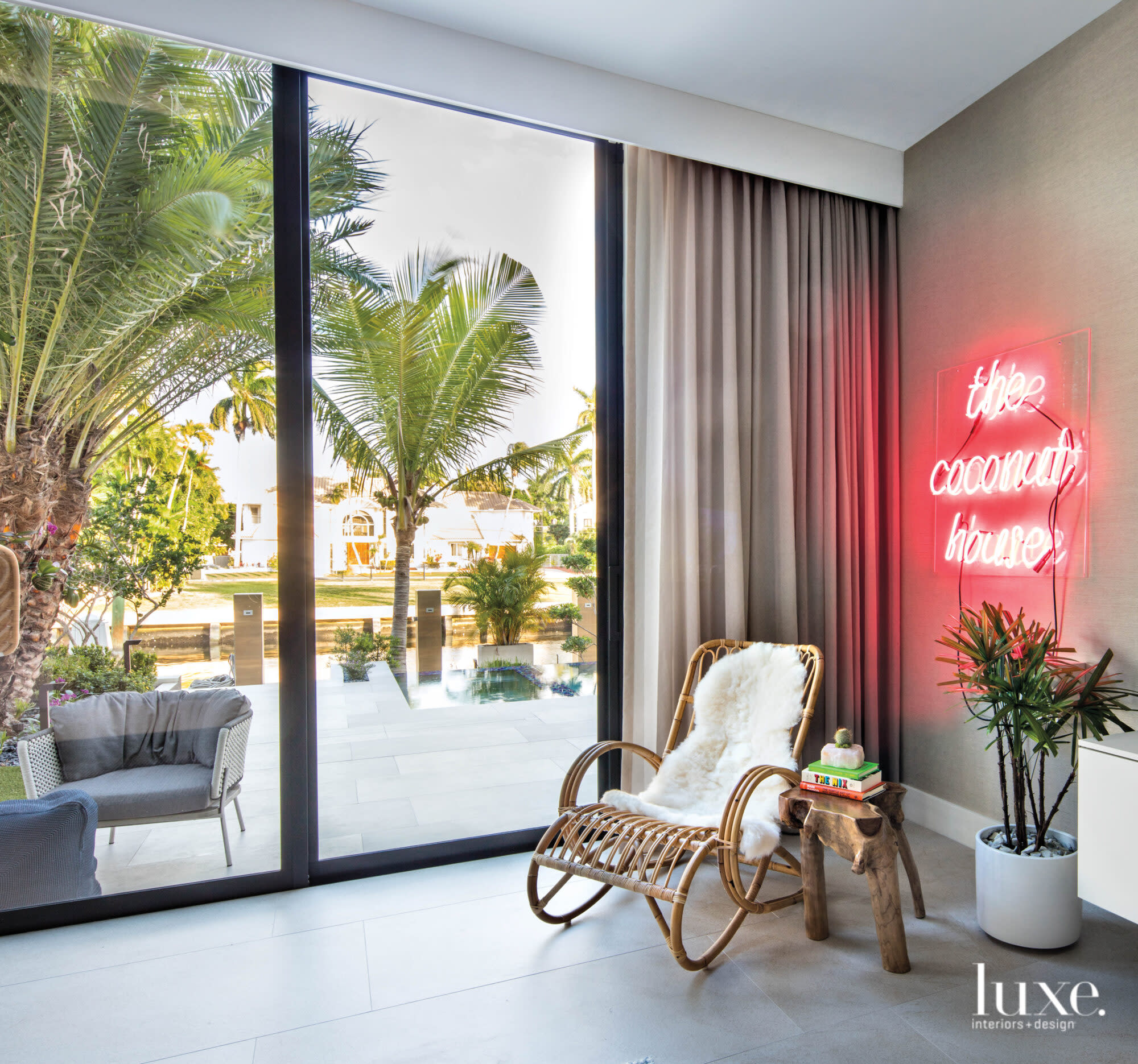 Guest bedroom with neon sign that says "The Coconut House" and a rattan chair.