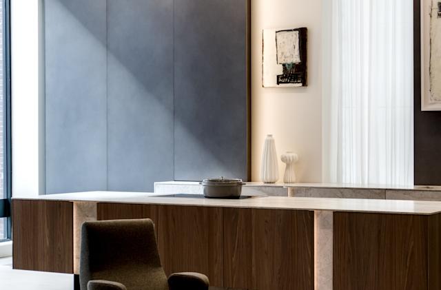 Modern kitchen interior with a minimalist design, featuring a wood and marble island. Artworks hang on a gray wall, with soft natural light filtering in.