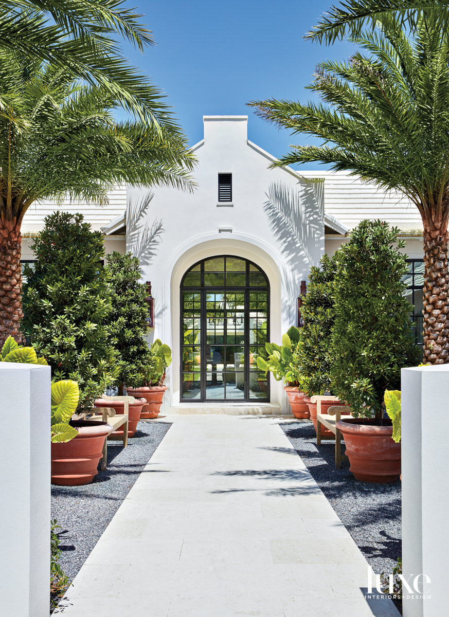 white bermuda-style house with a path to front door lined with trees